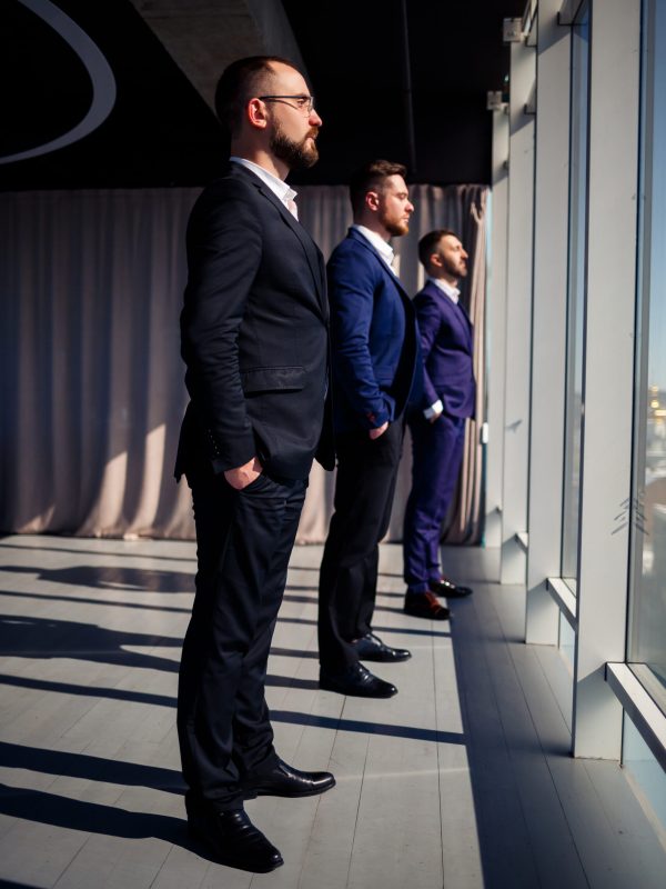 Three successful businessmen stand in a row and look out the window overlooking the city in a large skyscraper
